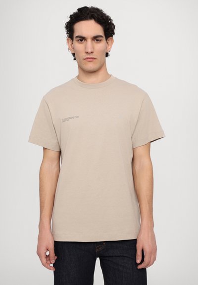 Tricou din bumbac bej cu guler rotund, mâneci scurte și un mic detaliu de text pe partea stângă a pieptului. Purtați-l cu blugi negri.