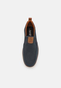 Chaussure slip-on marine avec un dessus texturé, une pièce en cuir marron et une semelle en caoutchouc. Taille 42 imprimée sur la semelle intérieure.