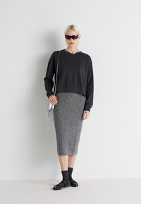 Svart avkortet genser med sølv detaljer, parret med en strukturert grå strikket blyantskjørt. Svart sokker og slip-on sko med nagler.