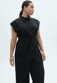 Svart jumpsuit med korta, strukturerade ärmar, krage och knytband i midjan. Har en slät tygkonstruktion och en avslappnad passform genom benen.