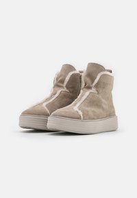 Bottines en suède beige avec un revêtement en fourrure blanche, dotées d'une fermeture éclair sur le côté et d'une semelle plateforme texturée de couleur beige clair.