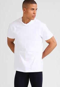 Witte katoenen t-shirt met een ontspannen pasvorm, korte mouwen en een v-hals ontwerp, gepresenteerd tegen een neutrale achtergrond.