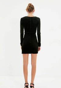 Černé sametové mini šaty s dlouhými rukávy, přiléhavý střih a jemný zip na zadní straně. Hladká textura s minimálním zdobením.