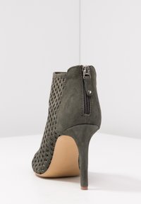 Zielony zamszowy botek za kostkę z perforowanym wzorem, wysokim szpilkowym obcasem i zamkiem z tyłu. Posiada gładką beżową podeszwę.