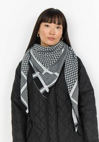 Mustvalge sall geomeetriliste mustrite ja ruudulise disainiga. Kandmiseks on see seotud kaela ümber musta tikandiga jope peal.