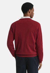 Roter gestrickter Pullover mit Rundhalsausschnitt und gerippten Bündchen, mit einer glatten Textur und in einfarbigem Design. Über einem kragenbetonten Hemd getragen.
