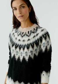 Pull en tricot avec un motif en noir, blanc et rose pâle. Il a un col rond et des manches longues avec une texture douce et duveteuse.