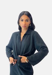 Zwarte textuur knoopsluiting shirt met lange mouwen, geknoopt op de taille. Heeft een kraag en een losse pasvorm.