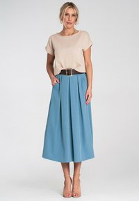 Beżowa bluzka z krótkimi rękawami, zestawiona z niebieską plisowaną spódnicą, zebrana brązowym paskiem. Gładki materiał i buty na kostkę dopełniają całość.