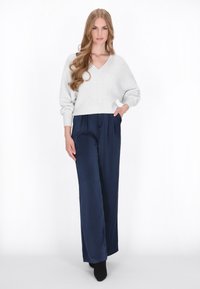 Lichtgrijze gebreide trui met een V-hals en verlaagde schouders, gecombineerd met marineblauwe broek met wijde pijpen en zijzakken, met een gladde textuur.
