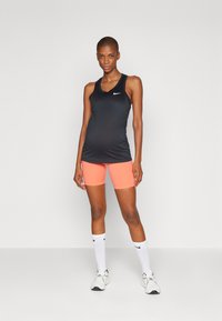 Svart ermeløs treningstop med rund hals, kombinert med rosa shorts. Hvitt Nike-logo på toppen. Hvit sokker og sporty sko.