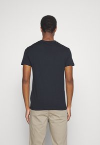 Camiseta negra de manga corta hecha de algodón, con cuello redondo y textura suave, combinada con pantalones beige claros.