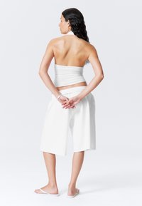 White strapless top and loose white shorts, featuring an elastic waistband, styled with white flip-flops and wavy dark hair.