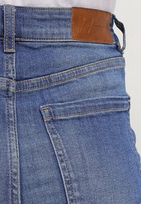 Höga blå denimjeans med en läderpatch i midjan, med kontrasterande sömmar och en avslappnad passform.