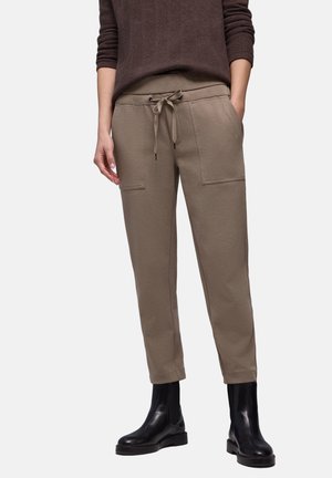 Kaki joggers met een taillekoord, twee steekzakken aan de voorkant, taps toelopende pijpen en een zachte textuur, gecombineerd met zwarte enkellaarsjes.