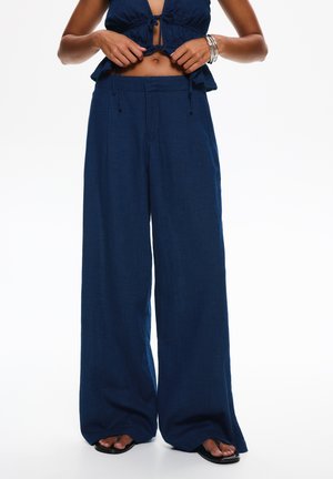 Námorné široké nohavice z ľahkej látky, s plisovaním vpredu a elastickým pásom, styled s čiernymi plochými sandálmi.