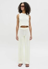 Kurzer, gehäkelter Strickoberteil und weite Hose in Off-White. Merkmale sind der gerippte Stoff, die taillierte Passform und der lockere Schnitt. Kombiniert mit braunen Flip-Flops.