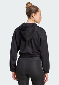 Sweatshirt noir à capuche en tissu texturé, coupe ample, avec taille élastique. Associé à des leggings noirs ajustés.