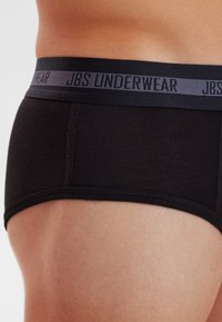 Sort bomuldsundertøj har en grå elastisk talje med "JBS UNDERWEAR" trykt. Stoffet er glat med flade sømme.