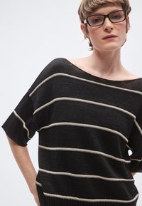 Μαύρο πλεκτό τοπ με ρίγες, ευρεία λαιμόκοψη και κοντά μανίκια. Διαθέτει οριζόντιες κρεμ ρίγες και άνετη εφαρμογή με ριμπ τελείωμα.