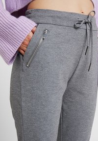 Grå sweatpants med dragsko i midjan, med stilrena sidofickor med dragkedja och ett mjukt, texturerat tyg. Mysig och åtsittande design.