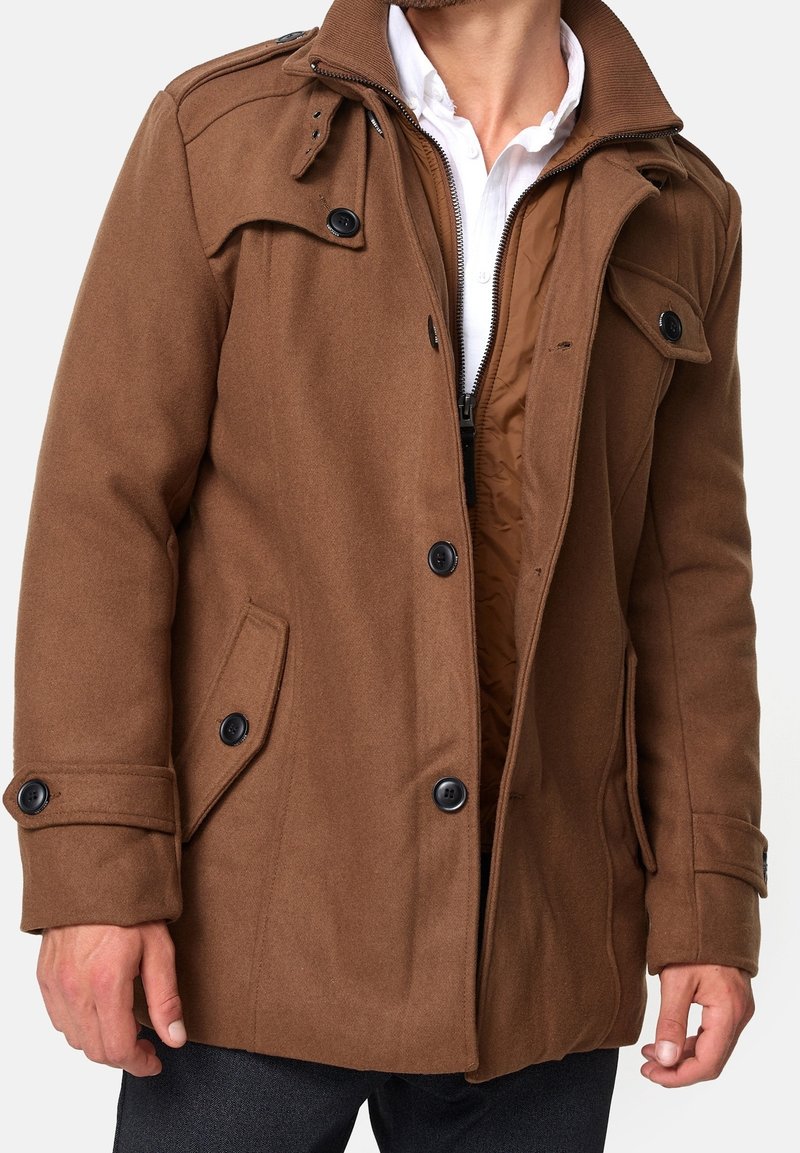 Manteau en mélange de laine marron avec une fermeture éclair à l'avant, des poches latérales et des poignets boutonnés. Présente une doublure intérieure matelassée et un col structuré.