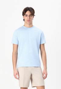 Lyseblå bomull T-skjorte med rund hals og korte ermer, kombinert med beige stripete shorts. Glatt tekstur og enkelt design.