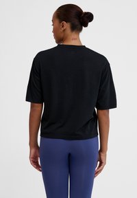 Sort kortærmet T-shirt med en afslappet pasform og rund halsudskæring, lavet af et blødt stof. Bæret med blå højtaljede leggings.