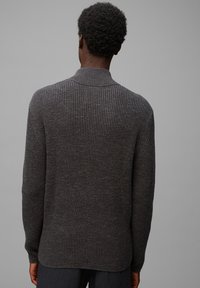 Ciemnoszara swetrowa bluzka z wysokim kołnierzem, z teksturowanym splotem i lekko zakrzywionym dołem, widoczna z tyłu.
