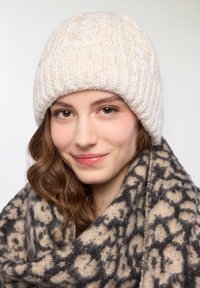 Biała dzianinowa czapka z teksturowanym, prążkowanym wzorem; zestawiona z wzorzystym beżowo-czarnym szalikiem z abstrakcyjnym wzorem.