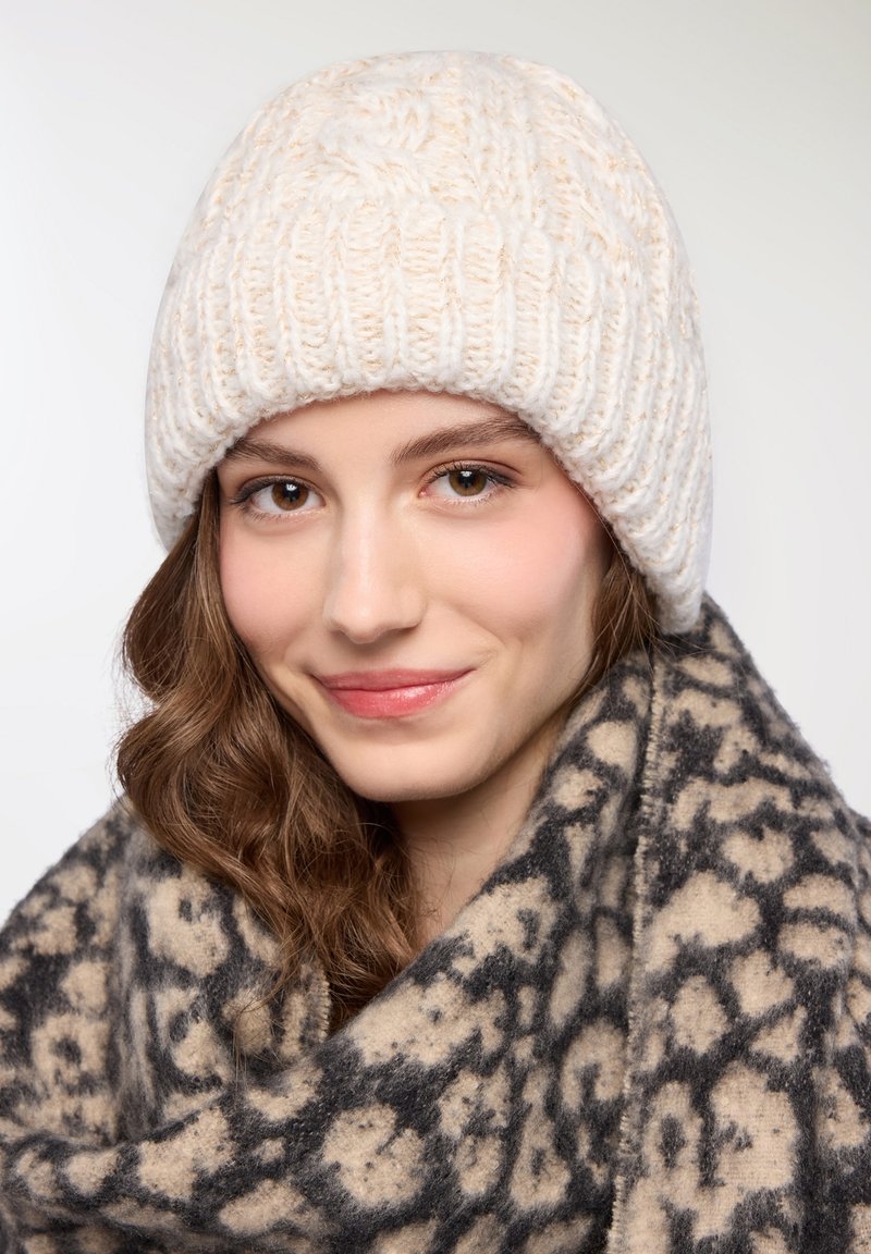 Biała dzianinowa czapka z teksturowanym, prążkowanym wzorem; zestawiona z wzorzystym beżowo-czarnym szalikiem z abstrakcyjnym wzorem.