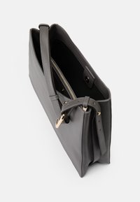 Sac fourre-tout en cuir gris avec une surface texturée, deux anses et un accent en métal doré. Poche zippée visible à l'intérieur.