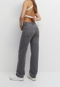 Jean en denim gris taille haute avec une coupe droite, doté de poches arrière et d'une texture subtilement usée, associé à des baskets blanches.