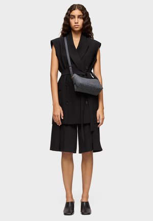 Vestido blazer negro sin mangas con cintura ceñida, combinado con pantalones cortos a medida. Acompañado de un bolso de hombro con un patrón oscuro y mules negros.