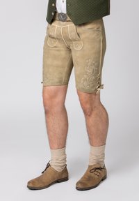 Beige leren shorts tot aan de knie hebben geborduurde bloemenpatronen, voorzakken en veters. Gecombineerd met beige gebreide sokken en bruine schoenen.