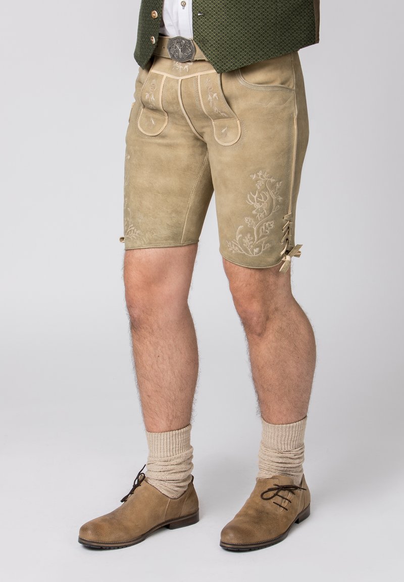 Beige leren shorts tot aan de knie hebben geborduurde bloemenpatronen, voorzakken en veters. Gecombineerd met beige gebreide sokken en bruine schoenen.