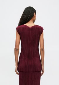 Πληθωρικό τοπ σε μπορντό από πλυμένες πτυχές με κοντά μανίκια, διαθέτει βαθύ V-ντεκολτέ και λεία υφή. Ο σχεδιασμός ρέει προς το ελαφρώς μακρύτερο πίσω στρίφωμα.