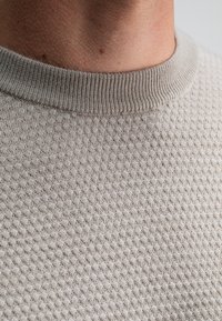 Close-up van de nek en beigerijpe gebreide trui met geribde kraag.