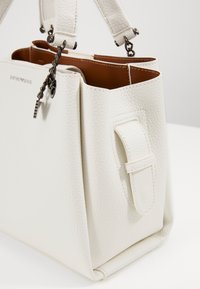 Vit läderhandväska med grynig yta, med brun insida, en sydd sidoficka och silverkedjedetaljer.