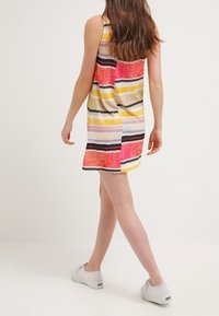 Randig ärmlös klänning med rosa, gula och svarta horisontella linjer på en ljus bakgrund; bärs med vita sneakers.