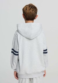 Felpa grigia con un grande cappuccio, texture morbida e strisce blu navy sulle maniche. Presenta una vestibilità comoda e polsini e orlo a coste.