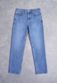 Μπλε τζιν παντελόνι με ίσια πόδια, κλείσιμο με κουμπί μπροστά και σχεδιασμό με πέντε τσέπες, απλωμένο σε γκρι τσιμεντένια επιφάνεια.