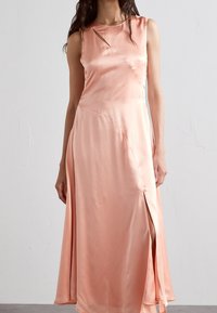 En ärmlös, knälång klänning i mjuk persikosatin har en rund halsringning, slits på sidan och vinklade utskärningar på bysten.