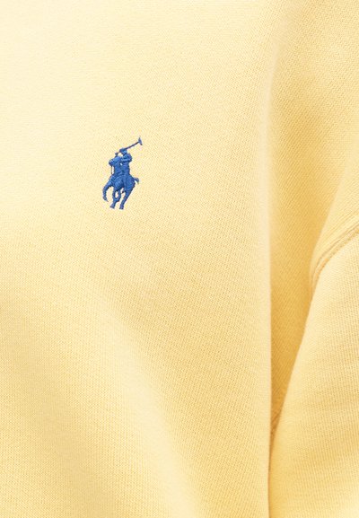 Yellow cotton sweater with a blue embroidered polo player logo. Features a textured fabric and ribbed cuffs. Close-up view highlights details.