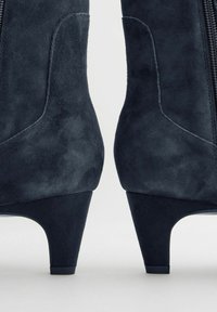Bottines en daim bleu foncé avec un talon effilé, dotées d'une fermeture éclair latérale, d'accents de design courbés et d'une texture lisse et mate.