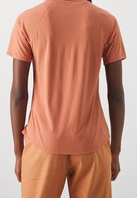 Camiseta de manga corta color óxido, confeccionada con una tela suave, con dobladillo redondeado y mangas raglán, combinada con pantalones a juego.