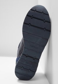 Suola di una scarpa blu scuro con un motivo di battistrada testurizzato e taglia 37 contrassegnata, posizionata contro uno sfondo bianco angolare.