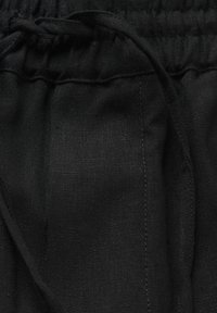 Zwarte stof shorts met een elastische tailleband en trekkoord. De textuur lijkt lichtgewicht en heeft een lichtjes gestructureerde uitstraling met zichtbare stikdetails.