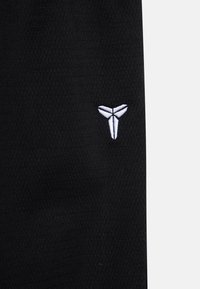 Black athletic garment featuring a textured fabric with a white embroidered logo on the side, showcasing a minimalist design.