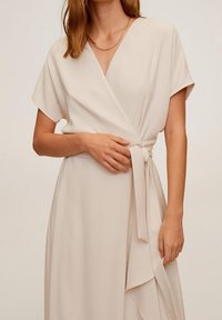 Robe portefeuille beige à manches courtes, décolleté en V et taille nouée. Tissu lisse avec un léger tombé et panneaux avant superposés.